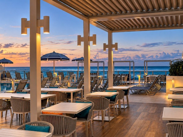 Sunset seaside patio with lounge chairs, umbrellas, and a pool under a pergola&mdash;ocean views and warm lights glowing.