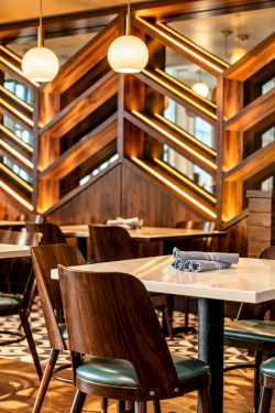 Cozy restaurant interior with green chairs, white-tablecloth tables, and warm backlit wooden lattice walls.