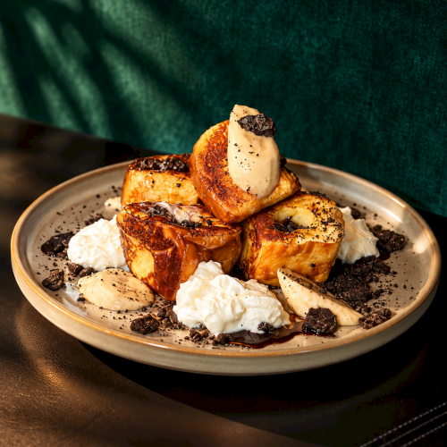 A plate of golden pastries with cream and poppy/chocolate crumbs on a green background.