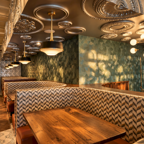 Cozy dining room with ornate ceiling lights and wood tables, plus a green mosaic-tile wall and booth seating.