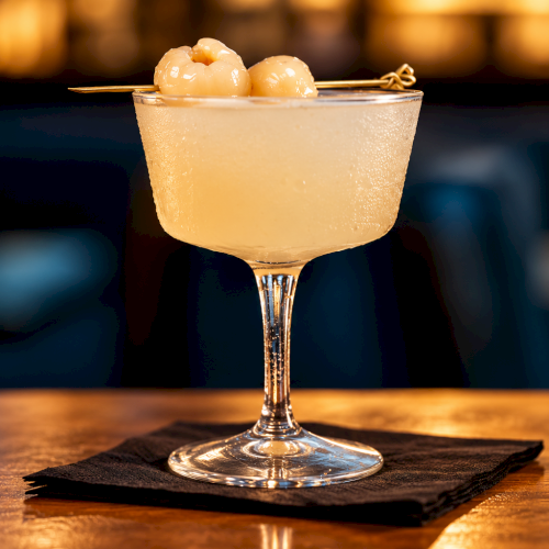 A chilled cocktail in a martini glass topped with two skewered olives, served in warm bar lighting.