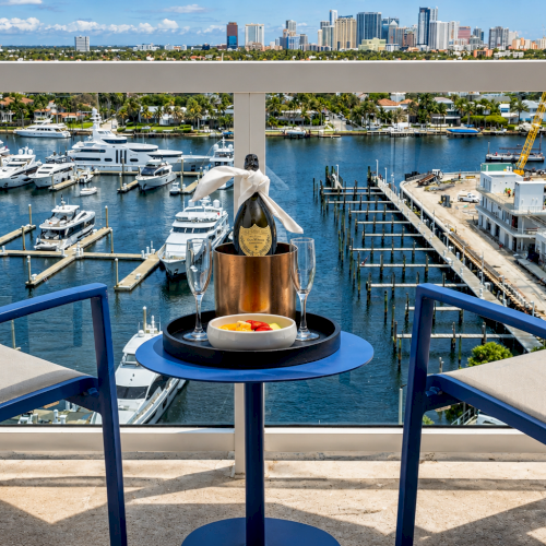Champagne on a patio table overlooking a luxury marina with yachts, palm trees, and a downtown skyline.