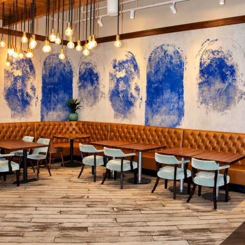 Warm restaurant interior with leather booths, wooden tables, hanging Edison bulbs, and blue abstract wall art.