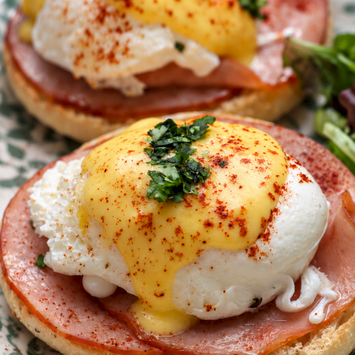 Close-up of eggs Benedict: poached eggs with hollandaise, ham, and herbs on toasted bread.
