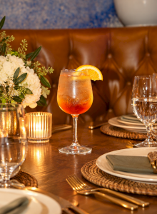 A sparkling orange-topped cocktail glass on a gold table with elegant flowers and dinnerware in a cozy setting.